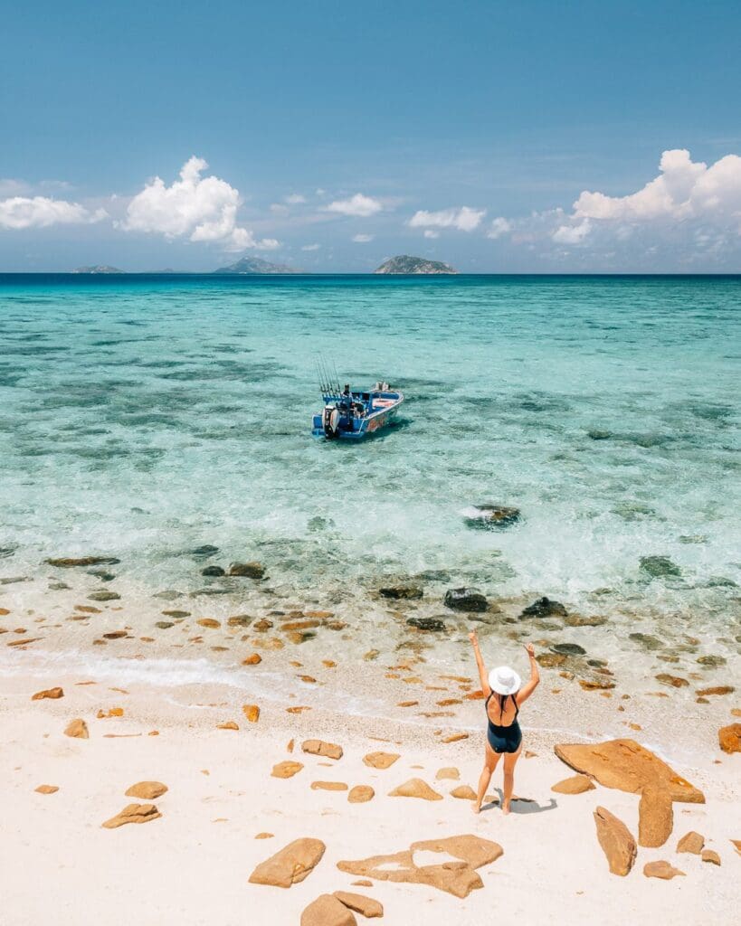 Woman on tropical beach with boat in background.