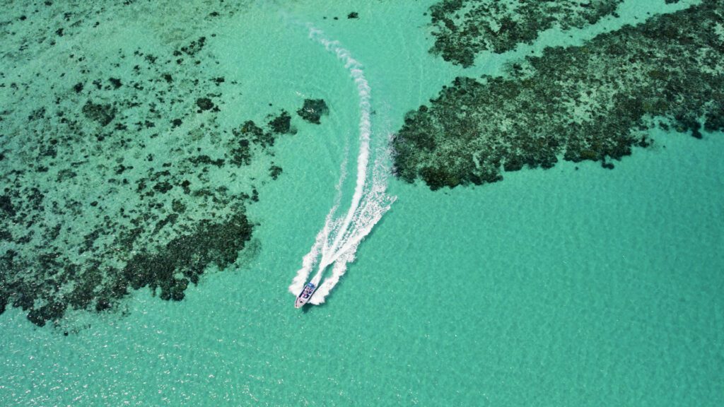 Circumnavigating Lizard Island - drone shot of boat driving through coral passage.